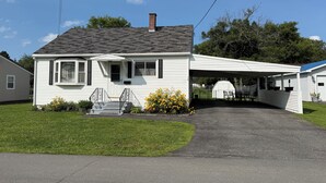 A single-story house with a covered porch, a front yard with a small flower bed, and a clear sky.