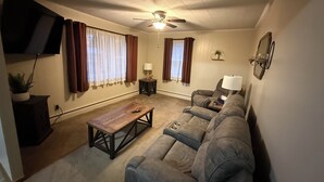 A living room with a sofa, a coffee table, a TV mounted on the wall, and a ceiling fan.