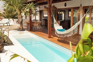 Ein Poolbereich mit Hängematte, Holzterrasse und Gartenmöbeln.