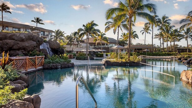 Ein Pool in einem Resort mit Wasserfall, Palmen und einer felsigen Landschaft.