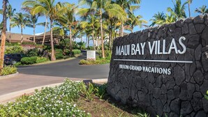 Schild für Maui Bay Villas, ein Teil von Hilton Grand Vacations, mit Steinmauer und tropischer Bepflanzung.