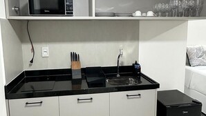 A compact kitchen with a microwave, sink, and black countertop. - Estudio Aurea Bauten 202 (João Pessoa)