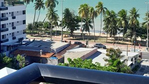 A view from a balcony overlooking a beach with palm trees and a clear blue sky. - Estudio Aurea Bauten 202 (João Pessoa)