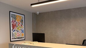 A reception desk with a sign reading "AUREA," a framed artwork on the wall, and a security camera above the desk. - Estudio Aurea Bauten 202 (João Pessoa)