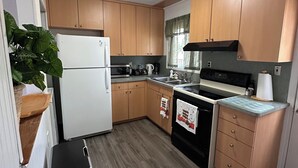 Cocina compacta con armarios de madera, un refrigerador blanco, estufa y pileta.