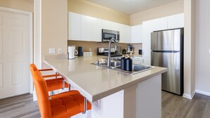 A modern kitchen with a central island, stainless steel appliances, and orange bar stools. - Charming Family Home | Heart of OC | Free Parking (Orange)