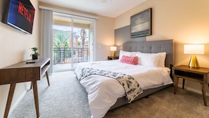 A hotel room with a bed, bedside tables, a desk, a ceiling fan, a painting, and a view of the outside. - Charming Family Home | Heart of OC | Free Parking (Orange)