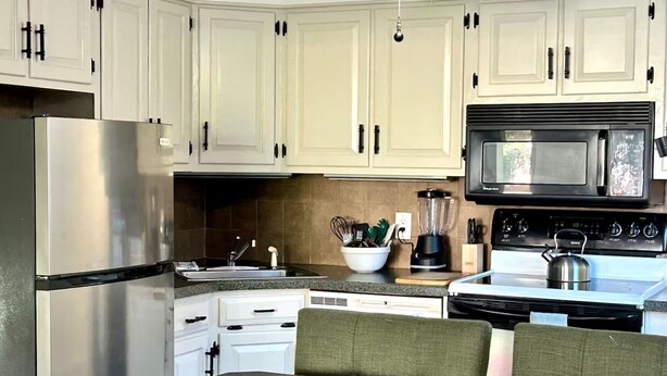 A kitchen with white cabinets, a stainless steel refrigerator, a black microwave, a stove, a dishwasher, and a dining table with chairs. - Litchfield Retreat, Wineries, Foliage & Skiing (Torrington)