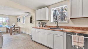 Een moderne keuken met witte kasten, een houten aanrecht en een raam met uitzicht op bomen.