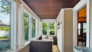 Eine überdachte Veranda mit Sitzgelegenheit, großen Fenstern und Blick ins Freie.