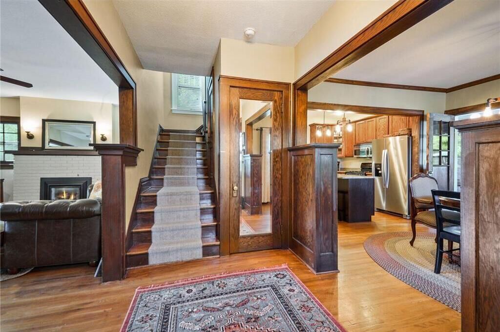A spacious living area with a fireplace, a staircase leading to another level, and a kitchen area with modern appliances.