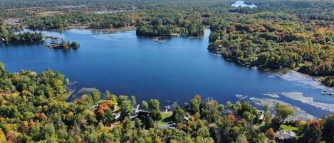 Un lago rodeado de bosque denso y algunos edificios.
