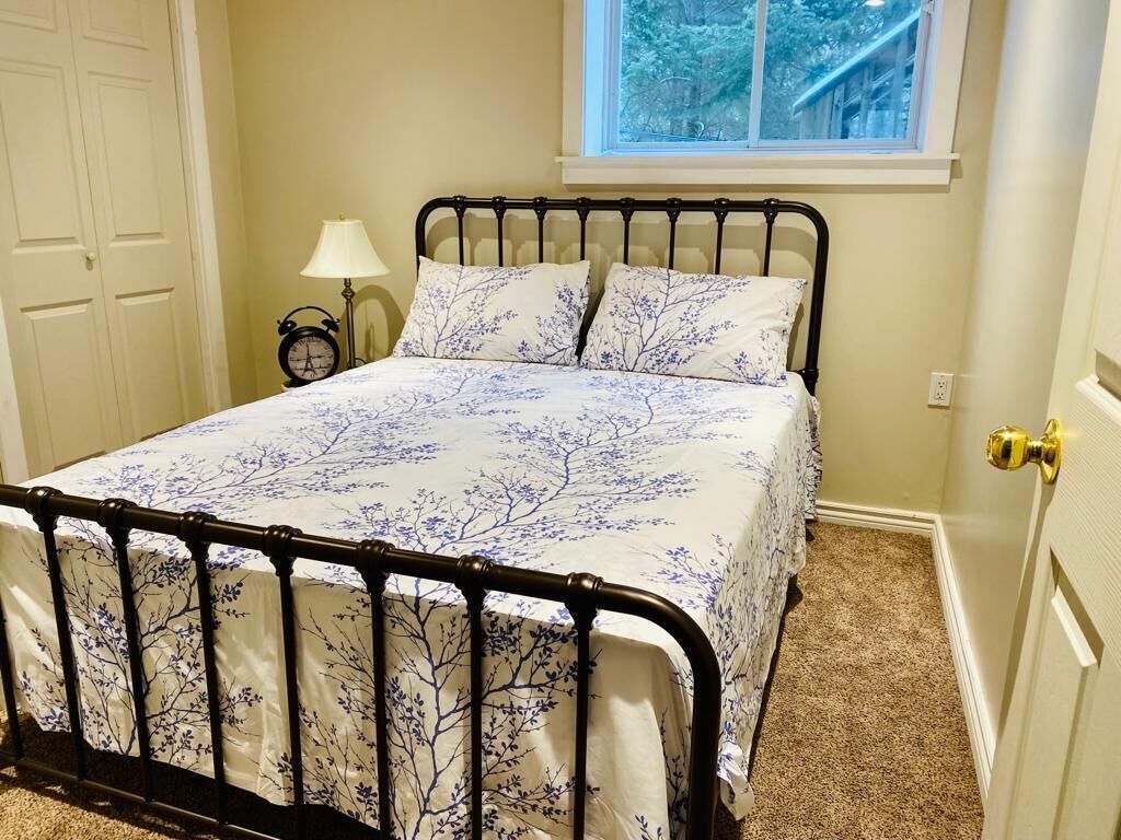 Un dormitorio con cama, mesita de noche, lámpara y ventana.