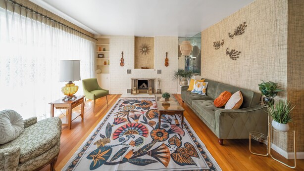 Un salon avec un tapis à motifs, un canapé vert, un fauteuil vert, une table basse en bois et une cheminée.
