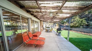 Une terrasse couverte avec un ventilateur de plafond, une table et deux fauteuils de jardin orange.