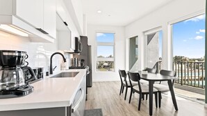 Cozinha moderna com ilha central, área de refeições com mesa e cadeiras, e varanda com vista.