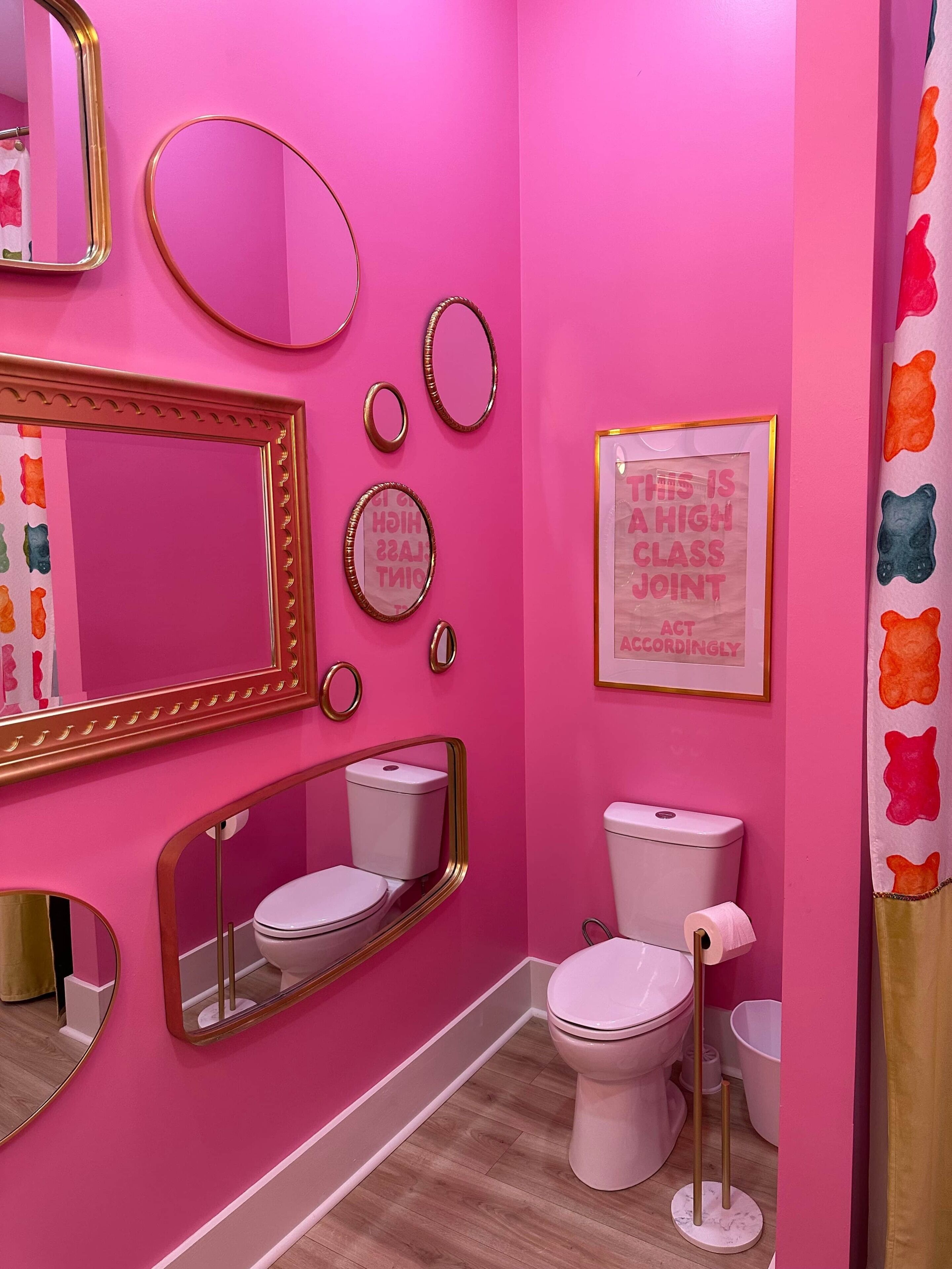 Ein Badezimmer mit rosa Wänden, zwei Toiletten, einem großen Spiegel und einem gerahmten Schild.