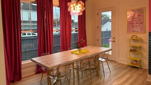 A dining area with a wooden table, clear chairs, a hanging light fixture, and a door leading outside.
