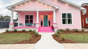 A pink house with a porch, a front door, and a small garden.