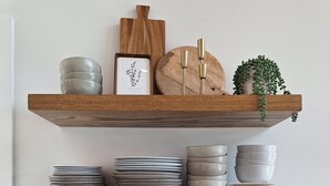 Une cuisine avec des étagères en bois où sont rangées des assiettes, des bols et des tasses, ainsi qu’une machine à café et une bouilloire.