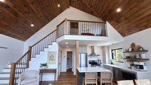 Une cuisine spacieuse dotée d’un îlot central, d’un escalier en bois et d’un coin repas avec un canapé et des fauteuils.