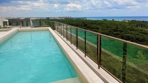 Une piscine rectangulaire dotée d’une balustrade en verre, entourée d’une végétation luxuriante et offrant une vue sur l’océan.