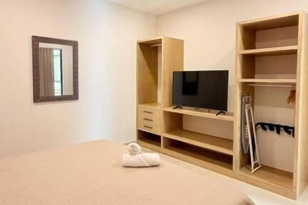 Une chambre à coucher avec un lit, un téléviseur posé sur une étagère en bois et un miroir accroché au mur.