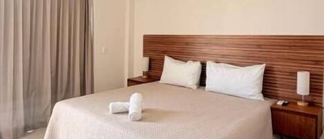 A neatly made bed with a wooden headboard, a bedside table, and a window with curtains.