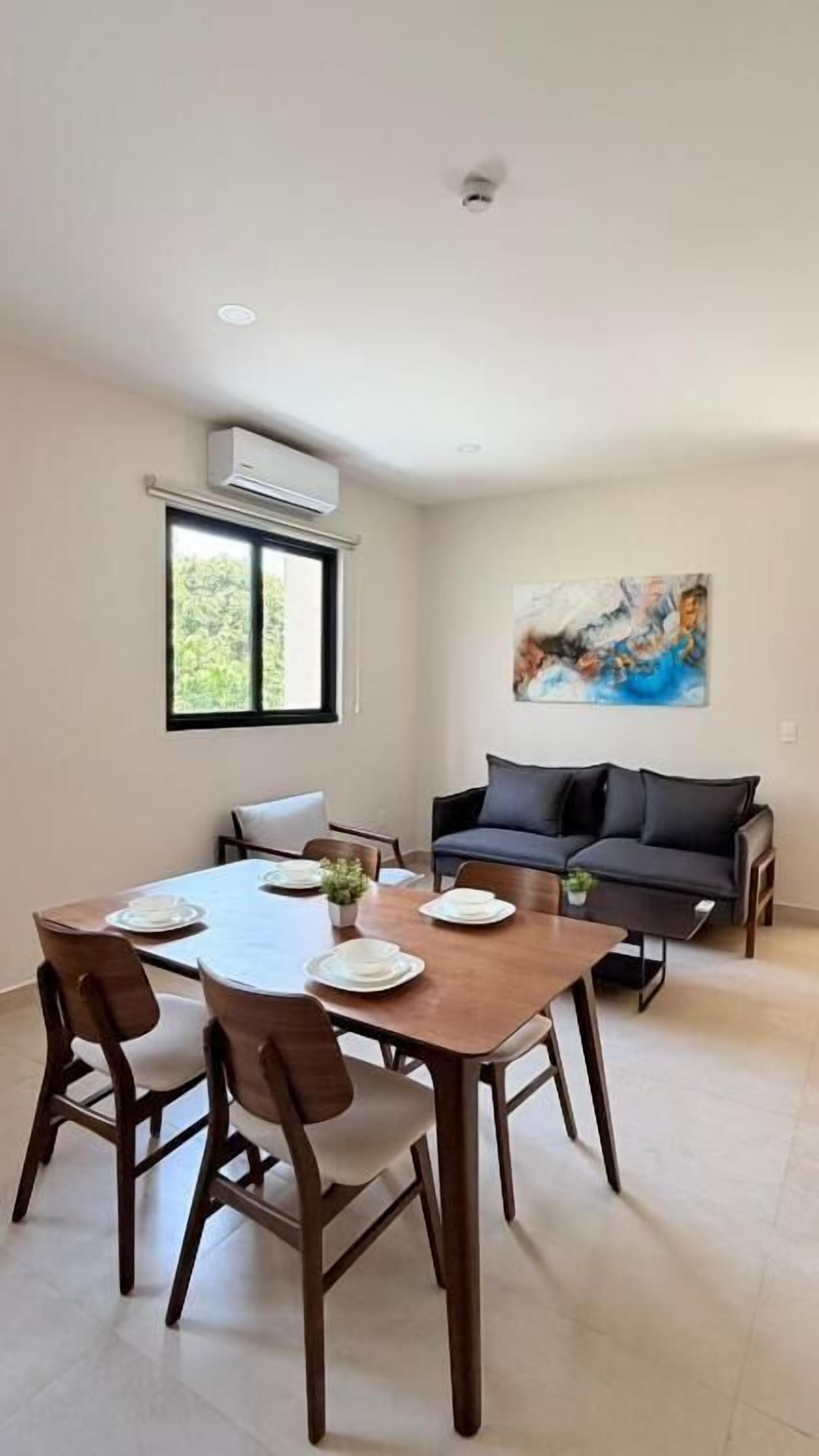 A dining area with a table set for four, a sofa, and a painting on the wall.