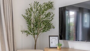 A living room with a wooden chair, a small potted plant, a framed welcome sign, and a TV on a wall. - Private 2-BR Suite w/ Patio (Mississauga)