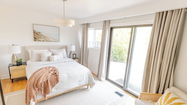 A modern bedroom with a large bed, bedside tables, a window with curtains, and a view of greenery outside. - Private 2-BR Suite w/ Patio (Mississauga)