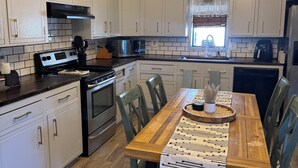 Une cuisine moderne avec des meubles blancs, une cuisinière noire et une table à manger en bois, accompagnée de chaises.