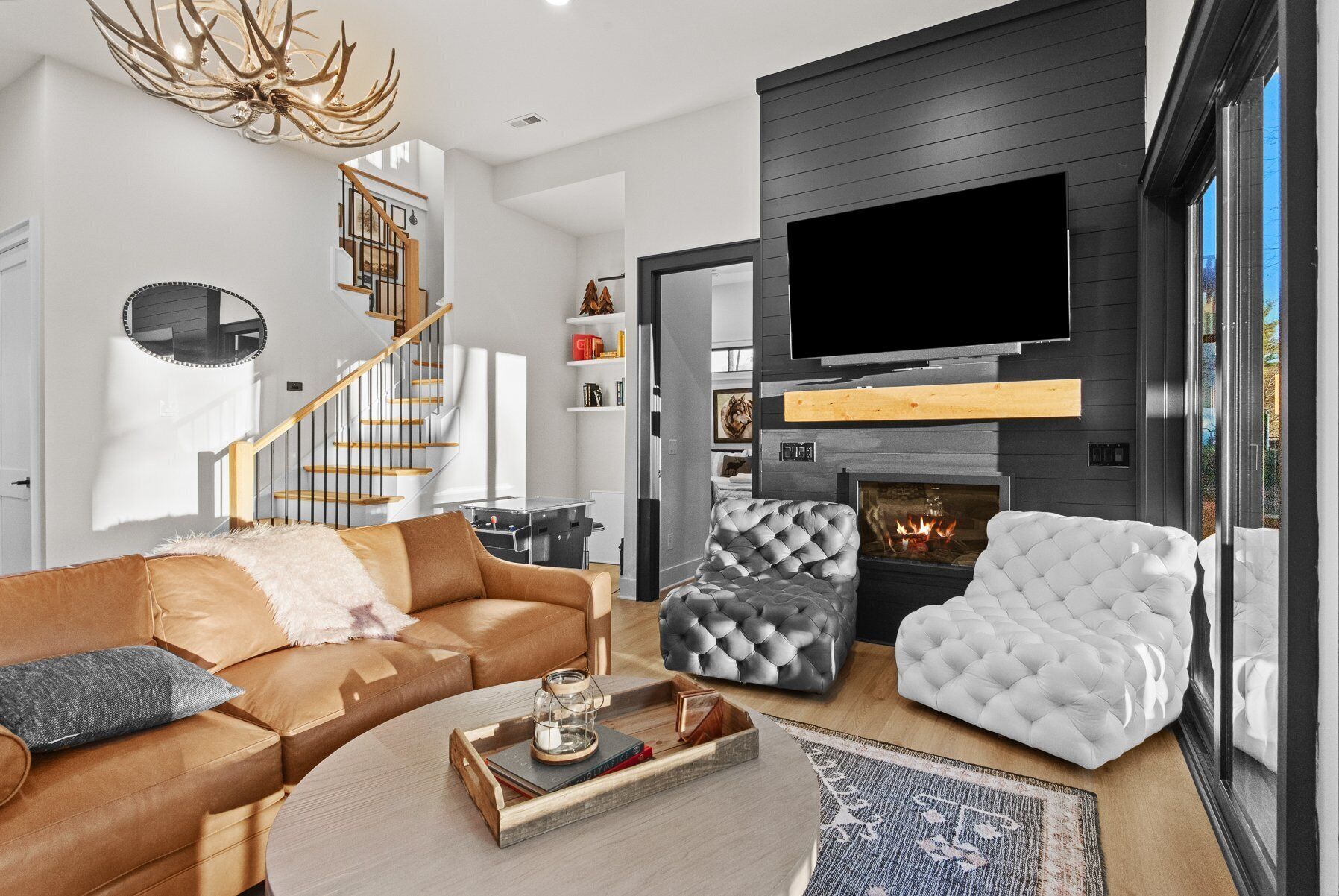 Ein modernes Wohnzimmer mit einem braunen Ledersofa, einem weißen, gepolsterten Sessel und einem grauen Hocker. Ein Flachbildfernseher ist über einem Kamin angebracht.