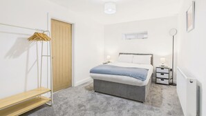 Une chambre à coucher comprenant un lit, des tables de chevet, un portant à vêtements, un radiateur et une porte.