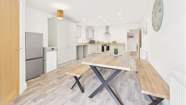 Une cuisine moderne avec des meubles blancs, une table à manger en bois et une horloge au mur.