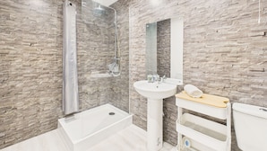 Une salle de bain moderne avec un mur à l’aspect pierre, une douche en verre, un lavabo sur colonne et un meuble-lavabo en bois.