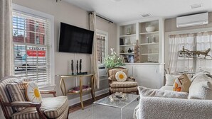 Ein Wohnzimmer mit Fernseher, gestreifte Stühle, einem Glastisch und einem Bücherregal.