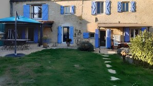 A two-story building with a tiled roof, blue shutters, and a covered outdoor seating area.