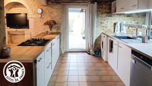 A kitchen with a stone wall, a wooden countertop, a gas stove, a washing machine, and a sink.