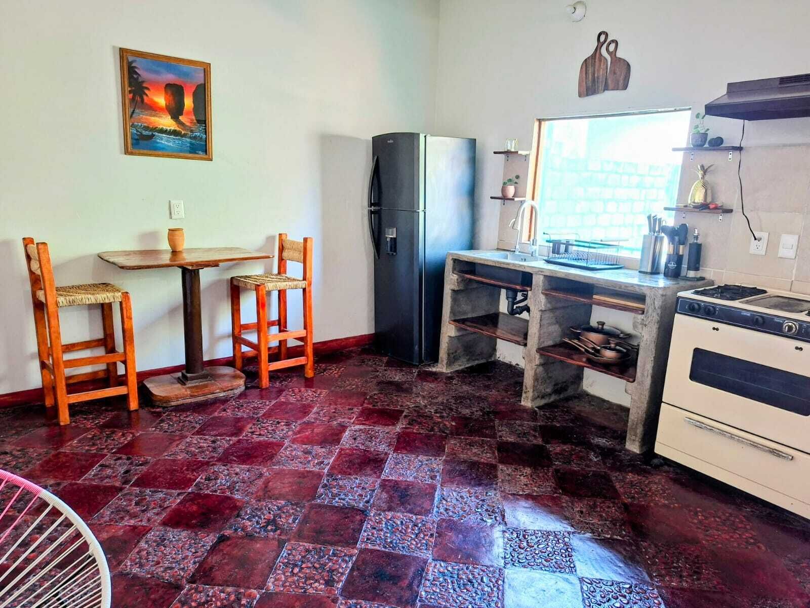 A compact kitchen with a refrigerator, a stove, a sink, and a dining area with two chairs and a table.