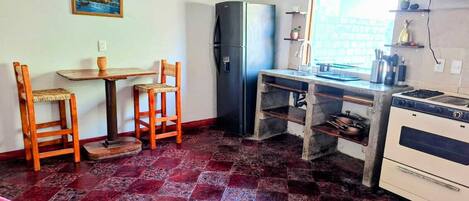 A compact kitchen with a refrigerator, a stove, a sink, and a dining area with two chairs and a table.