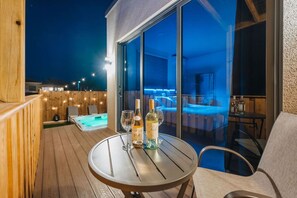 A wooden deck with a round table, two bottles of wine, and a glass of wine. A hot tub is visible in the background. - Private Suite w/HotTub, 2m Arikok Park, 3 people (Santa Cruz)