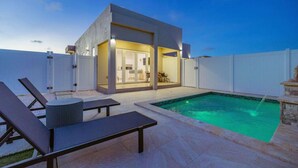Una casa moderna con piscina, mobiliario de exterior y un patio cubierto.