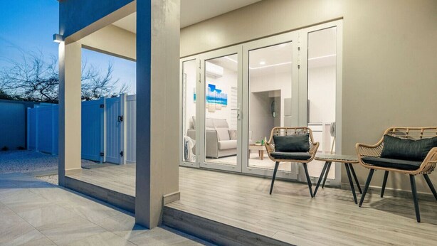 Un patio exterior moderno con zona de estar cubierta, una puerta corrediza de vidrio que da a un espacio interior y piso de concreto.