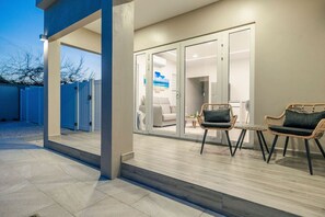 Een modern buitenterras met een overdekte zithoek, een schuifpui naar een binnenruimte en een betonnen vloer.
