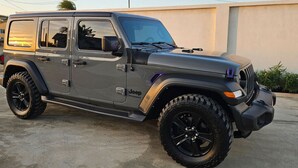 Un Jeep Wrangler gris con rines negros estacionado frente a un edificio.