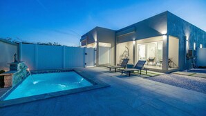 Una casa moderna con piscina, mobiliario de exterior y un patio bien iluminado.