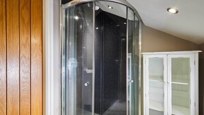 Un box de ducha con puertas de vidrio, un mueble blanco con puertas de cristal y una pared revestida de paneles de madera.