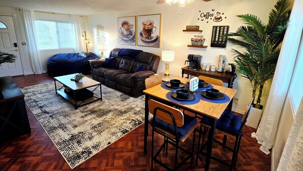 A cozy living room with a dark brown sofa, a coffee table, and a dining area with a wooden table and chairs. - Cozy Elevated Luxury - King Bed, Coffee Bar, Sleeps 5 (Springfield)