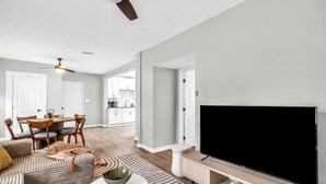 Een moderne woonkamer met een grote flatscreentelevisie, een bank, een salontafel en een eethoek met stoelen en een tafel.